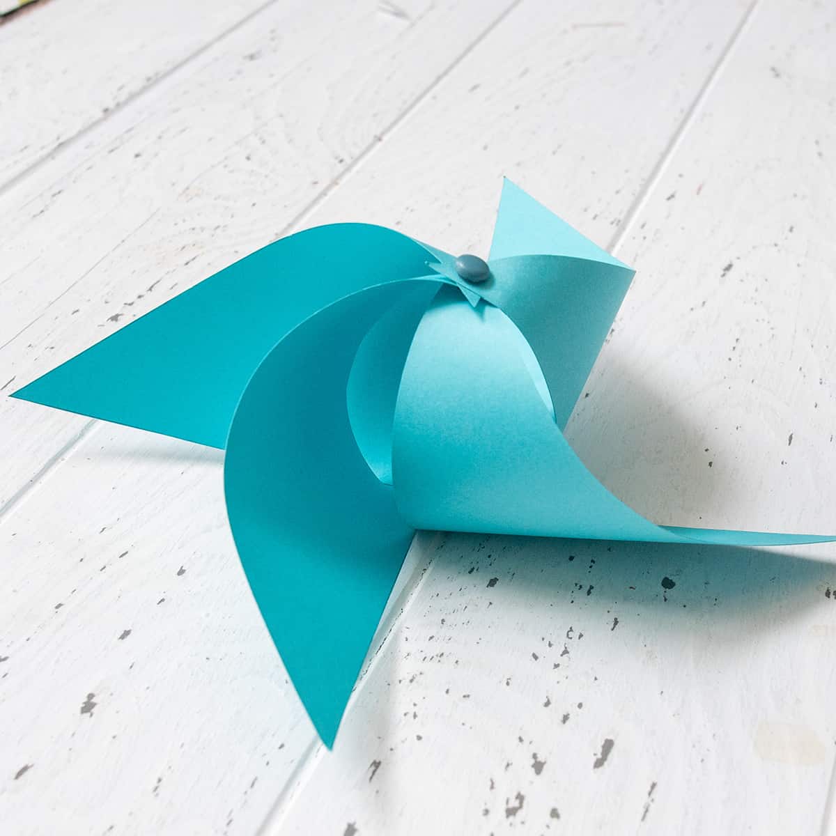 Colorful craft paper partially folded into DIY pinwheel shape on white surface.