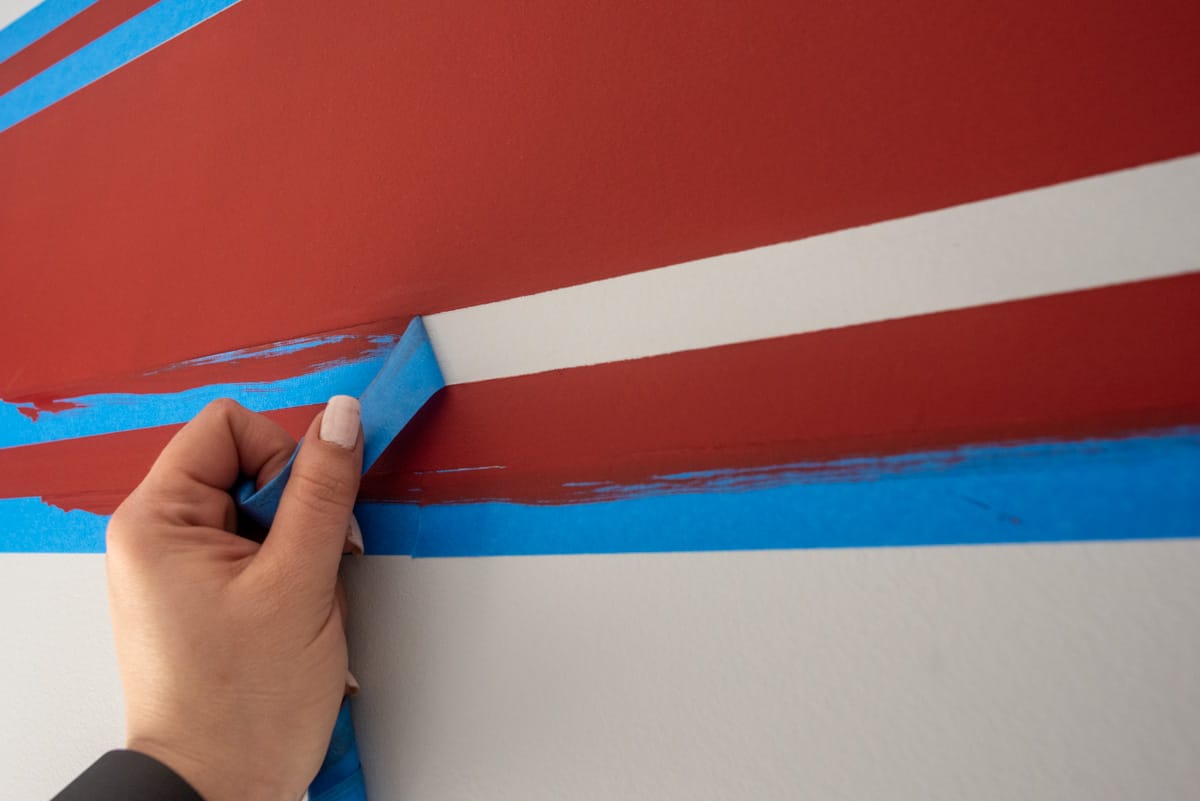 Woman pulling painter's tape away from painted wall for sharp lines.