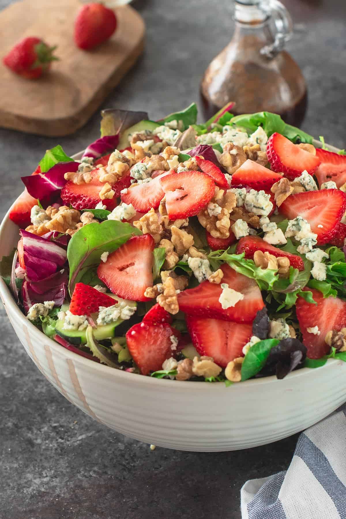 Strawberry Salad topped with whole strawberries, blue cheese, and walnuts with Glass dressing bottle of balsamic vinaigrette.