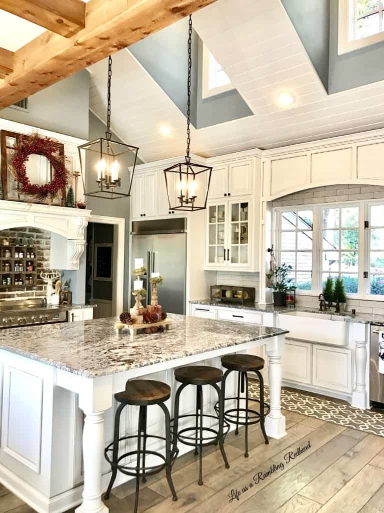 Large modern kitchen with high vaulted ceilings, white cabinetrs, and wide marble top island. 