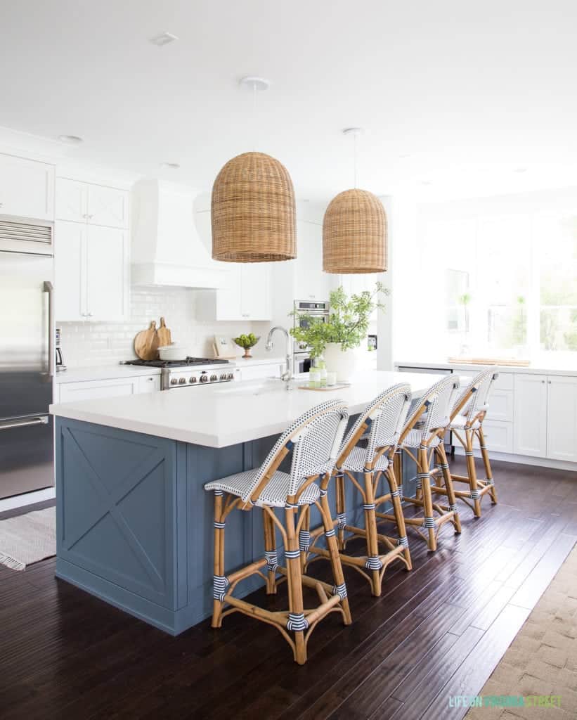 Spacious Open Kitchen with large blue island, white cabinets, dark wood floors, and wicker pendant lights. 