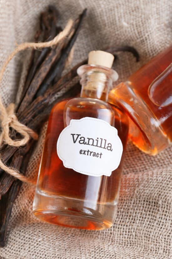 A bottle of homemade vanilla extract laying on burlap with vanilla bean pods next to it.