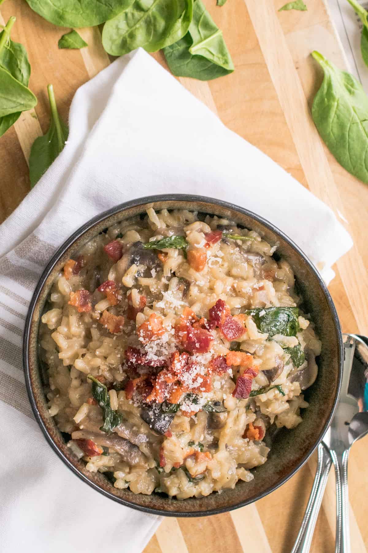 Bacon Mushroom Risotto with spinach in dark bowl on wooden cutting board,