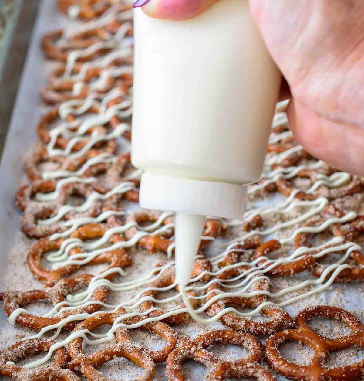 Cinnamon Sugar Pretzels with white chocolate being drizzled using a candy bottle to make perfect stripes.
