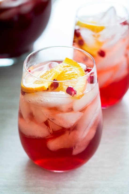 Vodka Punch in a wine glass with ice garnished with orange slices and pomegranate seeds.