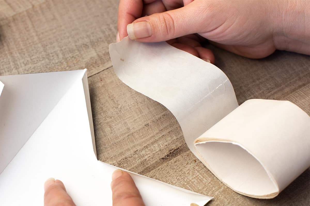 Woman holding glue dots to prepare to use them to adhere paper tabs.