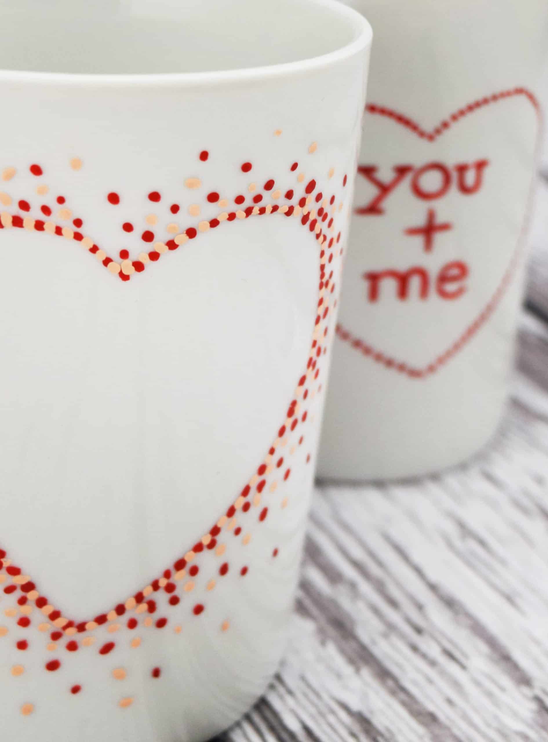 White ceramic coffee mugs with hand painted polka dot heart shapes on white wood planks. 