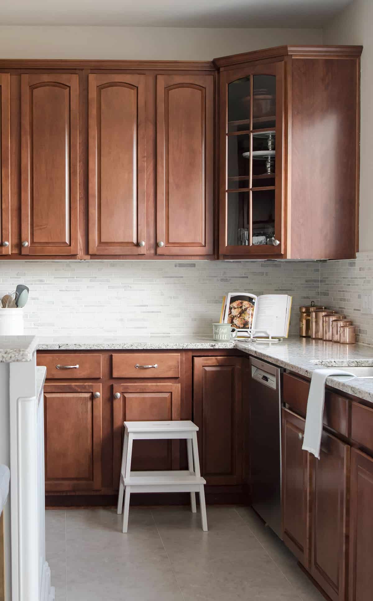 Dark wood cabinets in modern traditional kitchen makeover with light marble countertops, and light tile backsplash. 