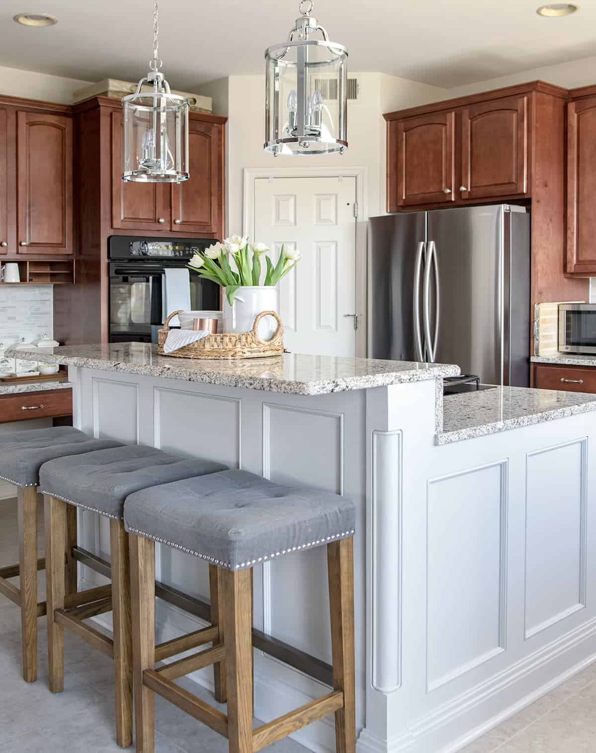 Modern Traditional Kitchen with Wood Cabinets and gray island, light marble countertops, pendant lights, and luxury vinyl floor. 