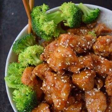 Chinese crispy honey sesame chicken over white rice and broccoli in a bowl.