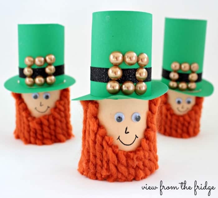 DIY leprechauns made from toilet paper rolls with bright green hats and orange yarn beard.