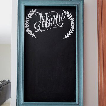 DIY chalkboard with white stenciled menu text and turquoise painted frame on gray wall in kitchen.