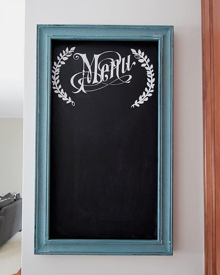 DIY chalkboard with white stenciled menu text and turquoise painted frame on gray wall in kitchen.