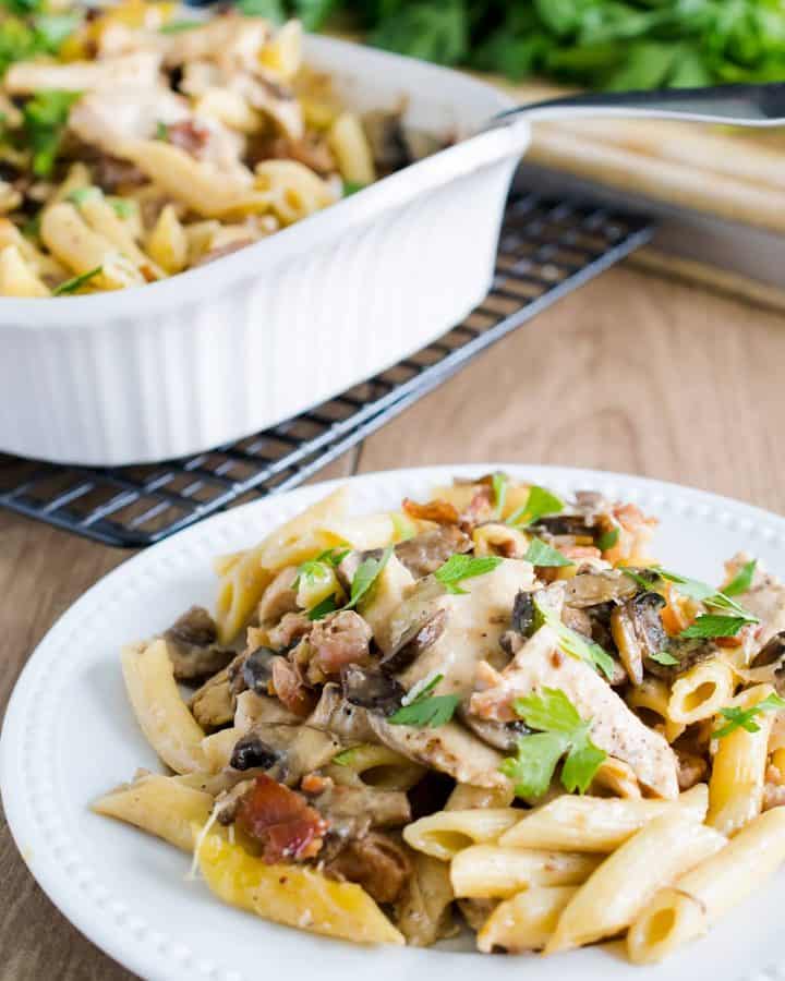 Chicken marsala pasta on a white plate in front of a serving platter.