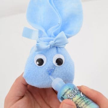 DIY blue felt bunny pouch with googly eyes held in hand painting glitter nose and mouth on front.