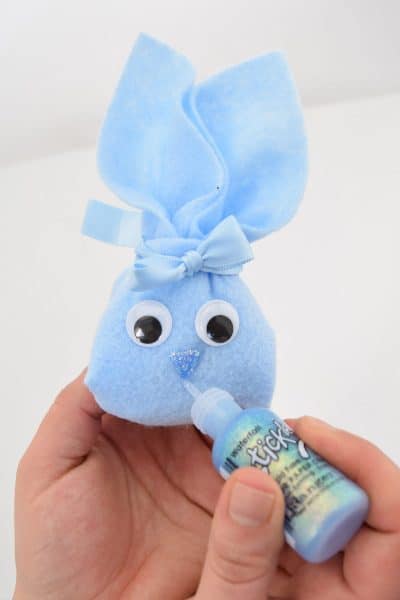 DIY blue felt bunny pouch with googly eyes held in hand painting glitter nose and mouth on front.