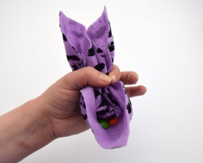 Hand holding folded purple felt pouch full of colored candies to create rabbit ear shape.