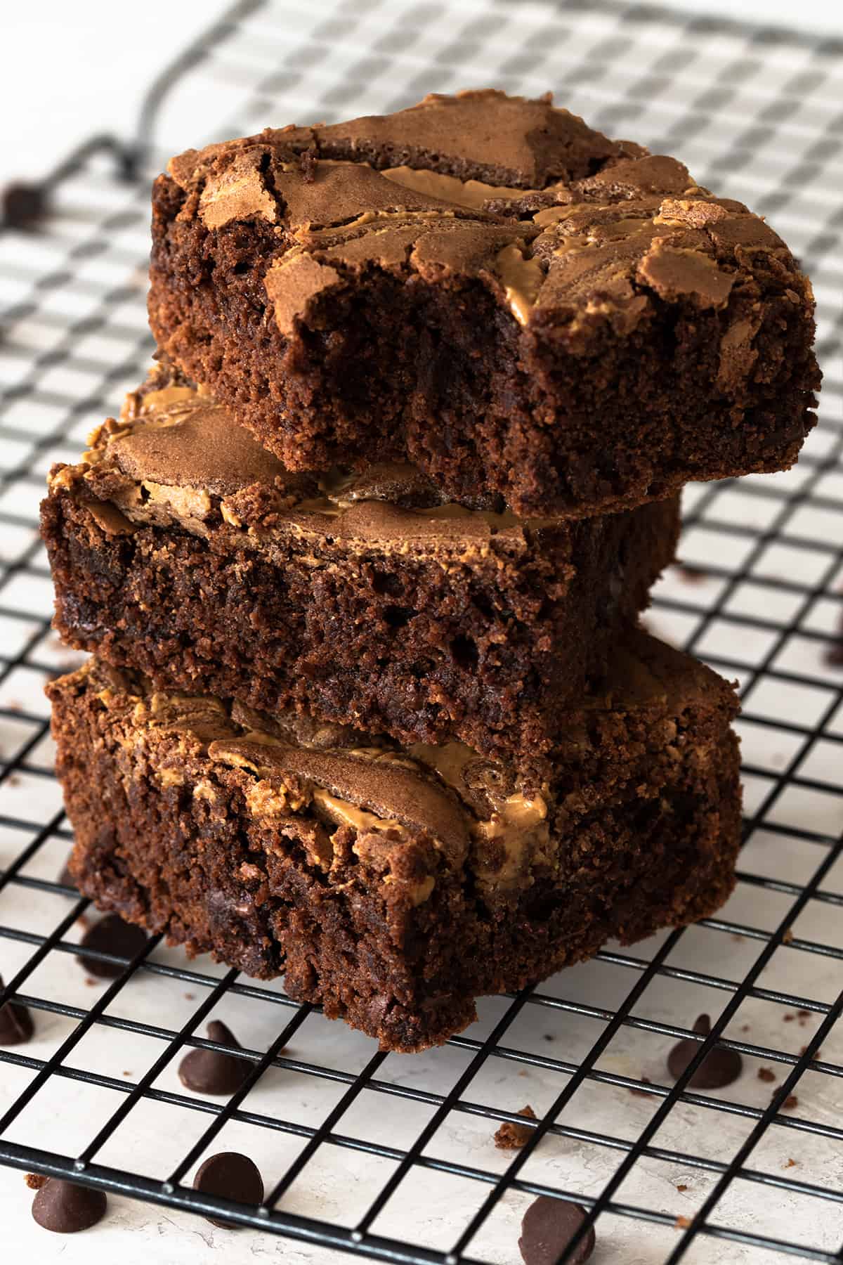 Three peanut butter brownies stacked on a cookie rack with chocolate chips around them.