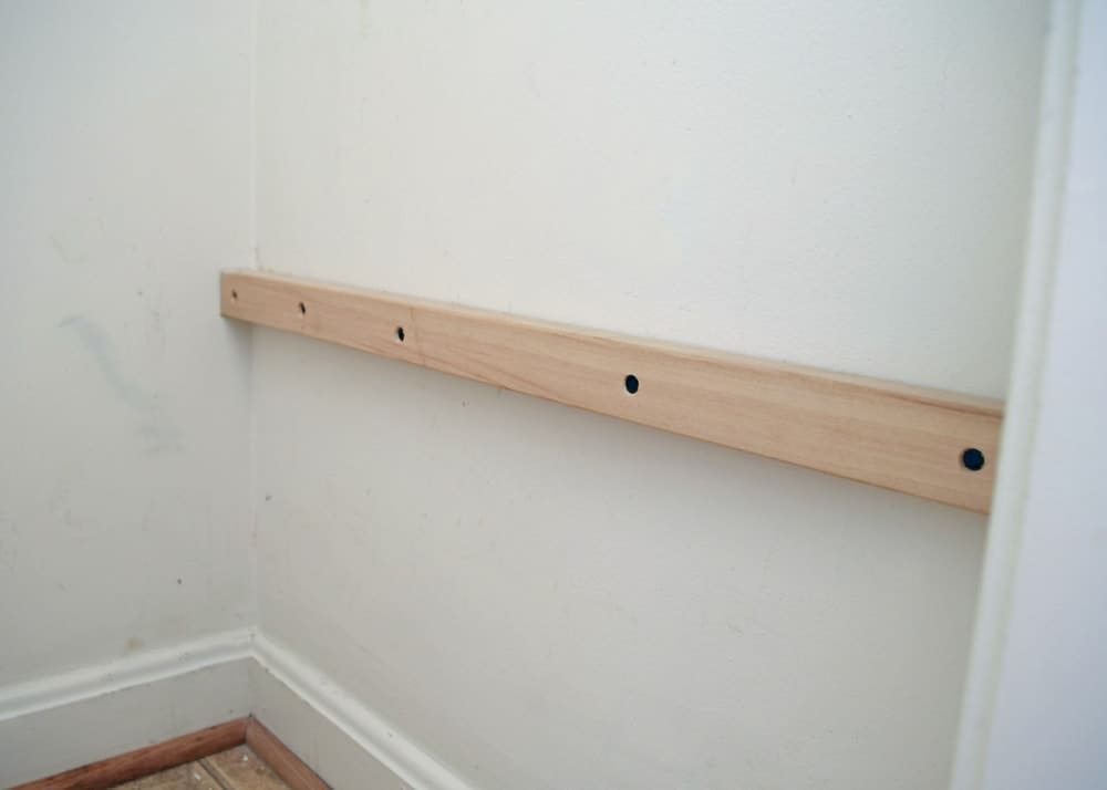 White wall in laundry closet with wooden rail mounted for adding shelves. 