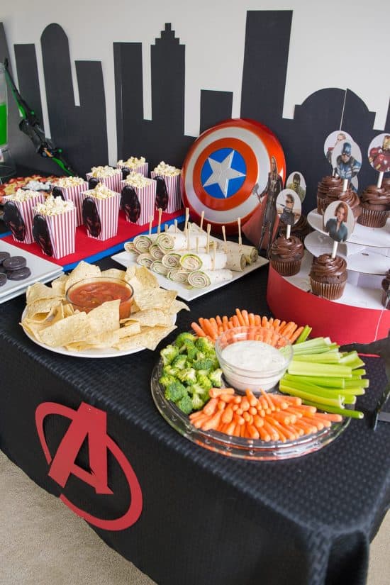 Avengers party table with decorations and food on a black table cloth.