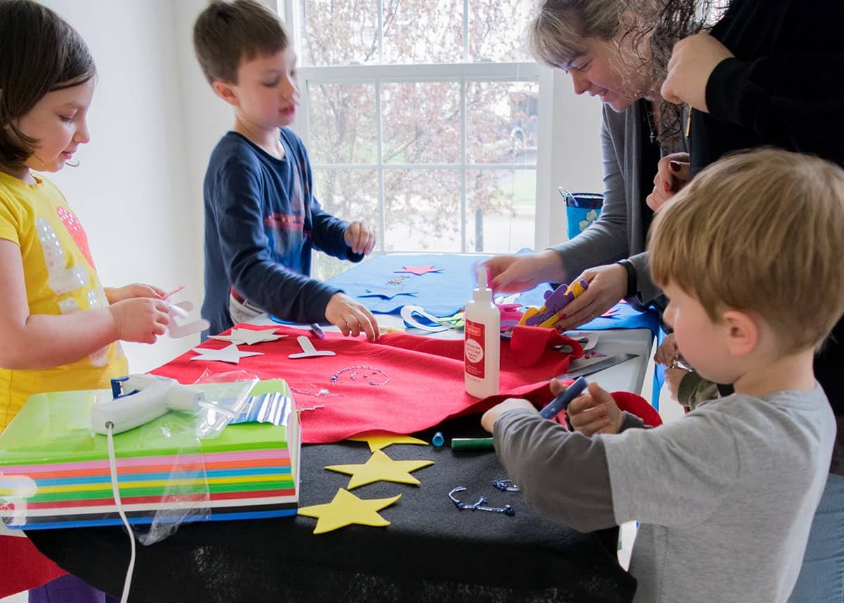 Children around table with fabric cutouts for making Avengers themed party decorations. 