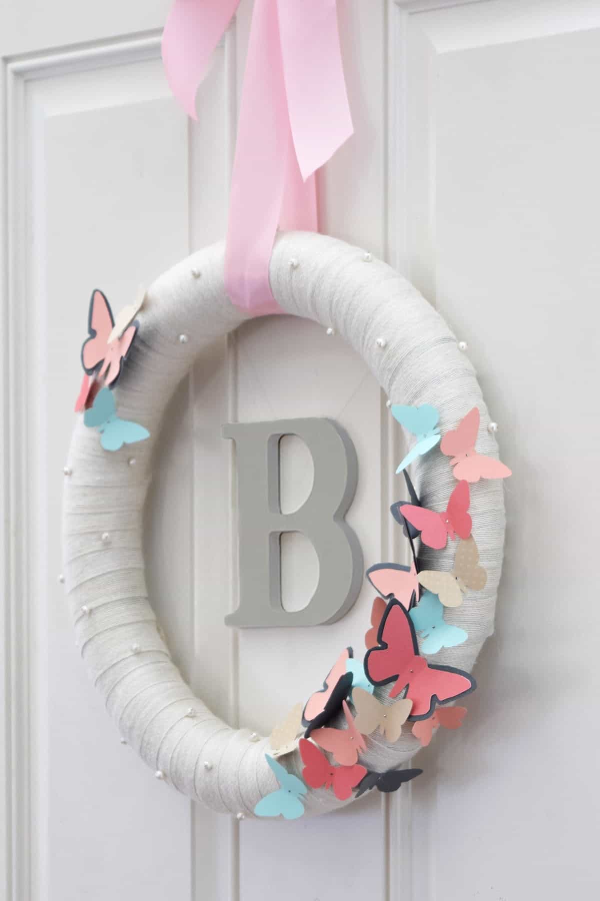 DIY Butterfly Wreath with Monogram on front door. Wrapped white wreath with blue and pink butterflies and pearls on pink ribbon.