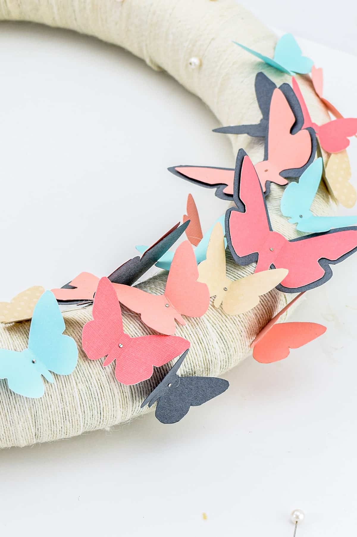 Colorful blue and pink paper butterflies attached to foam ring wrapped with white ribbon. 