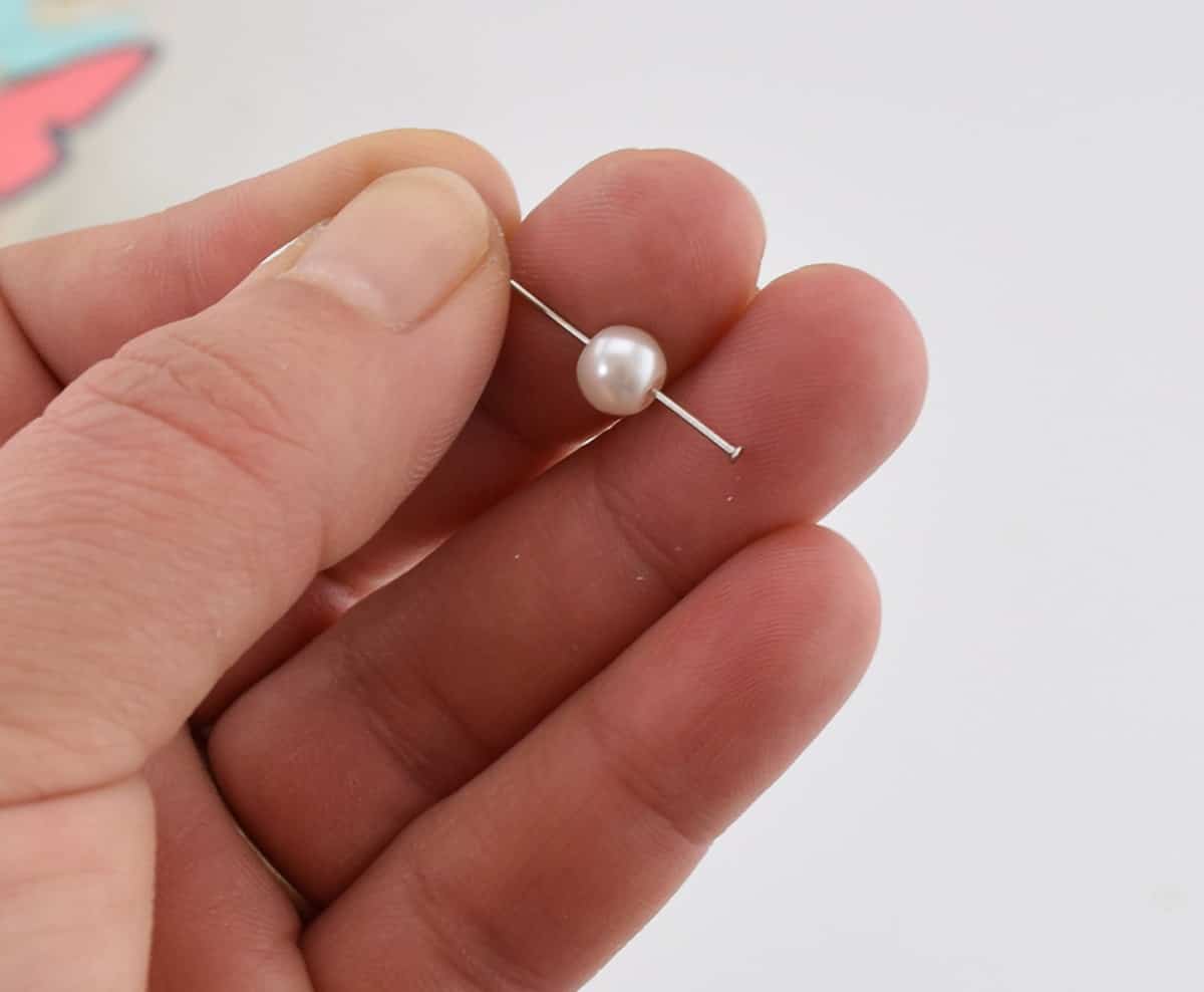 Hand holding white pearl with pin pierced through center with white background. 