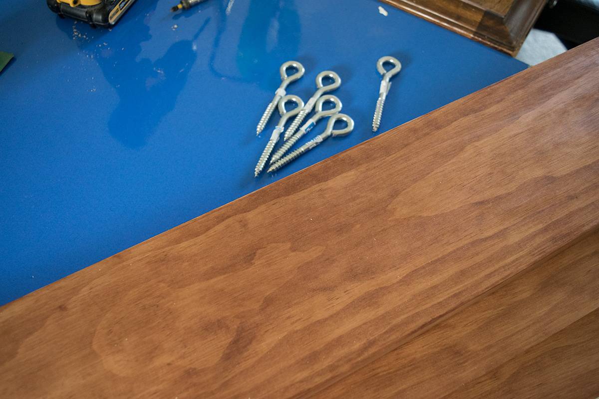 Wooden plank on blue surface next to pile of metal eyelet hooks.