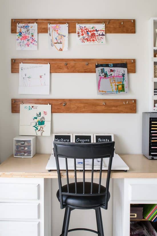 DIY wooden planks attached to white wall for hanging pictures at homework station in office.