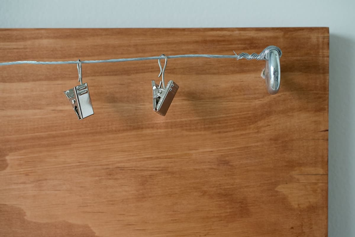 Wire mounted to stained wall plank with eyelet screw with hanging metal clips to hold artwork or photos.