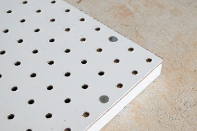 Shot of white painted peg board piece on concrete floor.