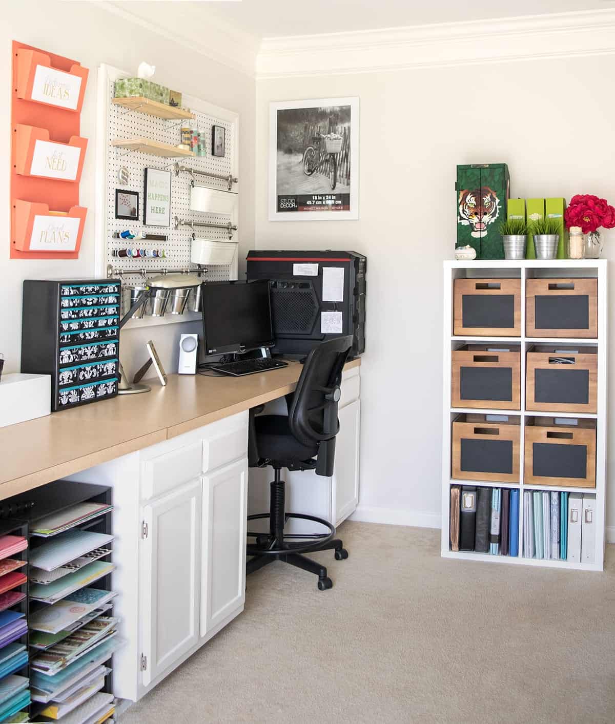 Corner area of organized white craft room with workstation, pegboard, and white shelf with wooden storage bins. 