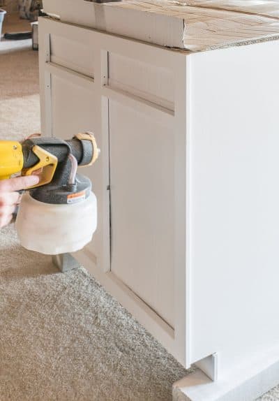 A paint sprayer being used on kitchen cabinets.