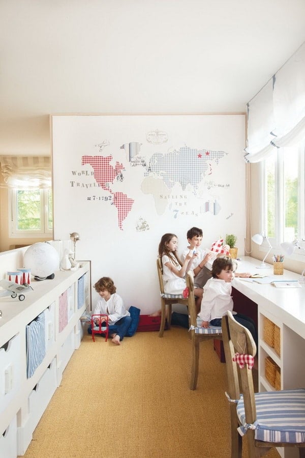 White playroom area with plenty of storage and desk space for completing homework with cute world map mural on wall. 