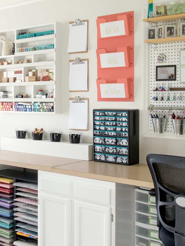 Colorful craft room with white walls and white cabinets with craft supplies on the wall and a pegboard.