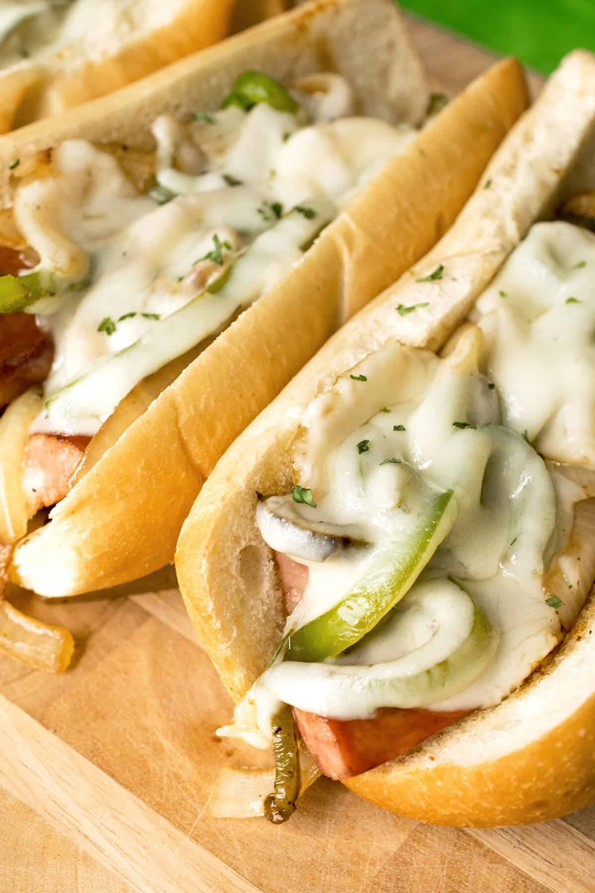 Kielbasa sandwiches with peppers, onions, and melted provolone on wooden surface. 