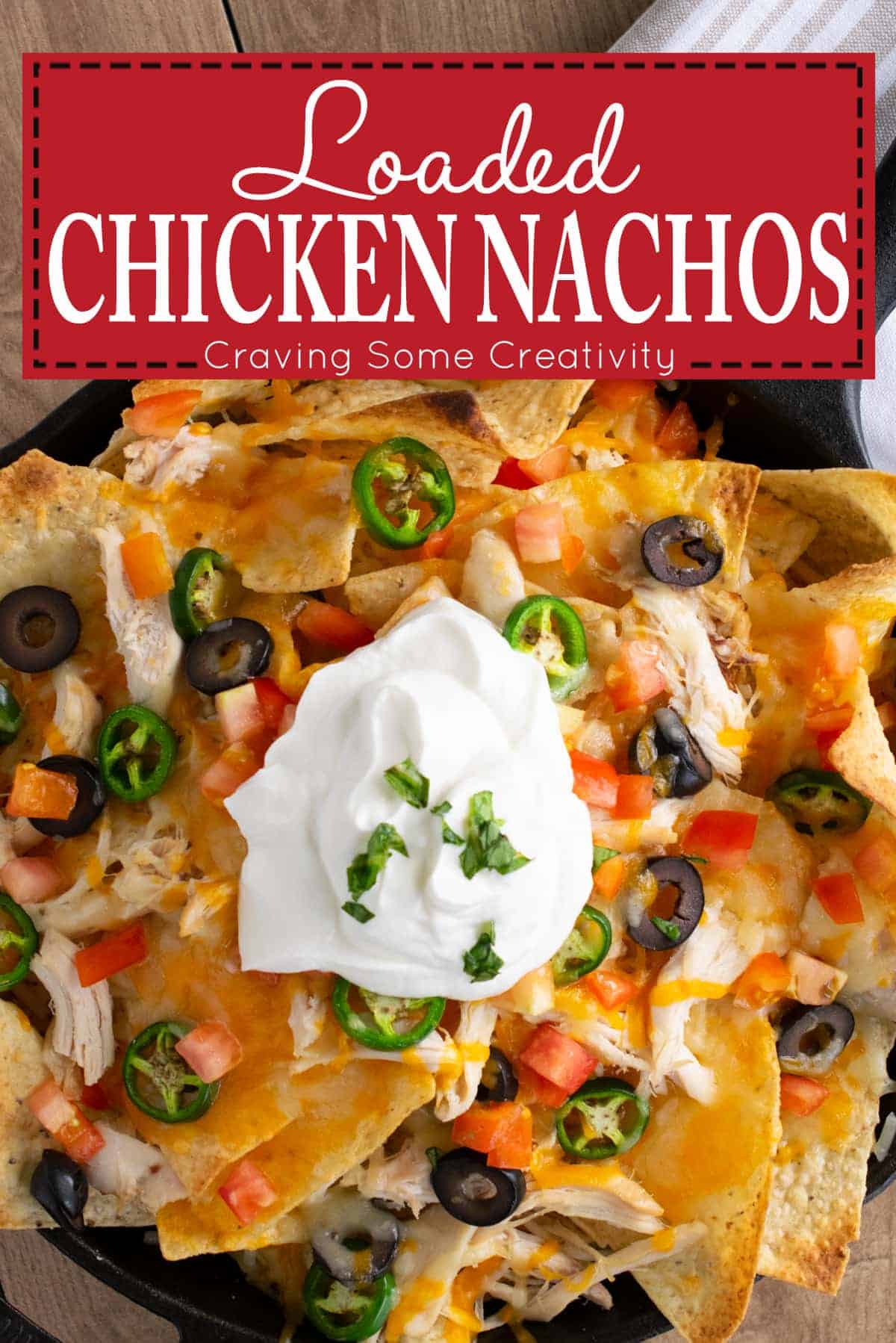 Easy Loaded Pulled Chicken nachos topped with melted cheese, black olives, diced tomatoes, jalapenos, and sour cream in cast iron skillet with post title. 