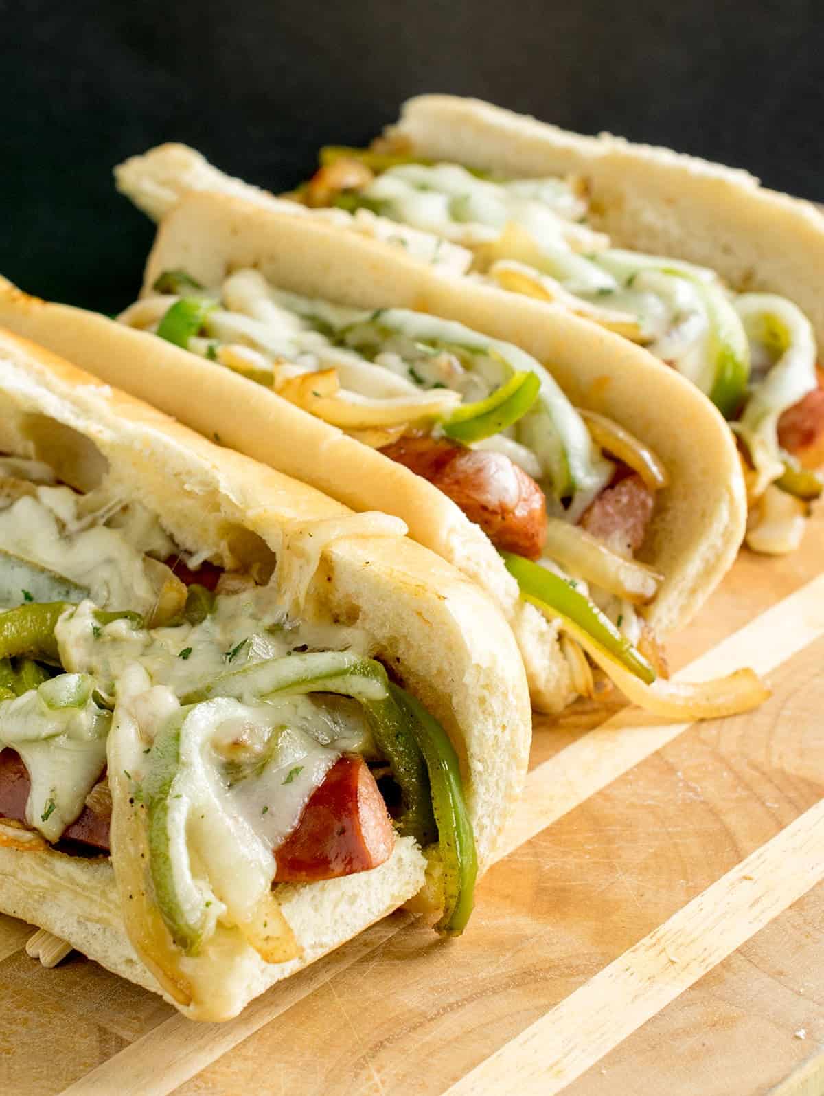 Kielbasa sandwiches with peppers and onions on fresh hoagie rolls with melted provolone on wood cutting board.