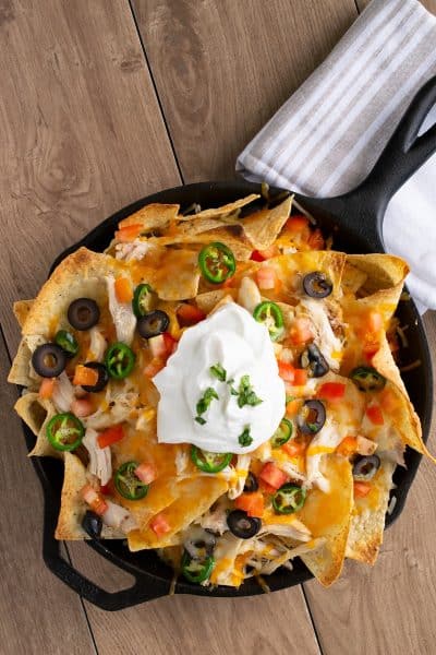 Shredded Chicken Nachos overhead with shredded Chicken, cheese, olives, pickled jalapenos and sour cream in a cast iron pan.