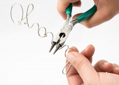 Hands using pliers to bend wire into cursive name an crimping together letters.