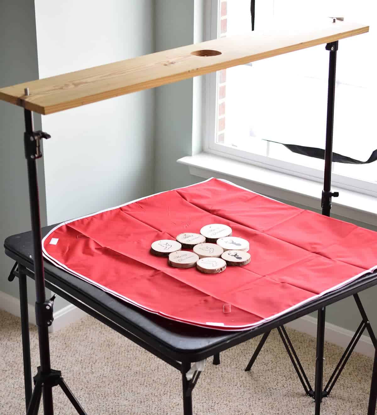 Table with red sheet and DIY ornaments with wood plank suspended over for taking overhead photos. 