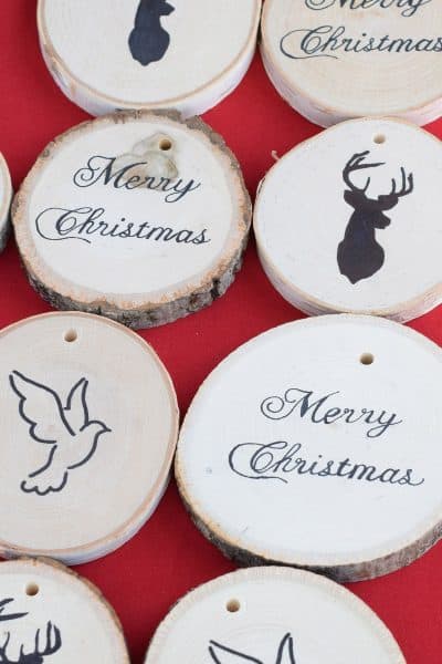 Two rows of wood slice ornaments with Christmas themed image transfers on red surface.