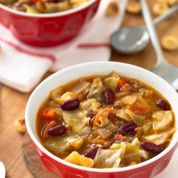 Cabbage Beef Soup in a red bowl on wood top with crackers.
