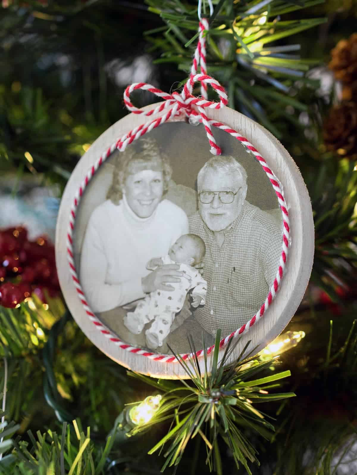 DIY round ornament with red and white ribbon detail hanging on Christmas tree. 