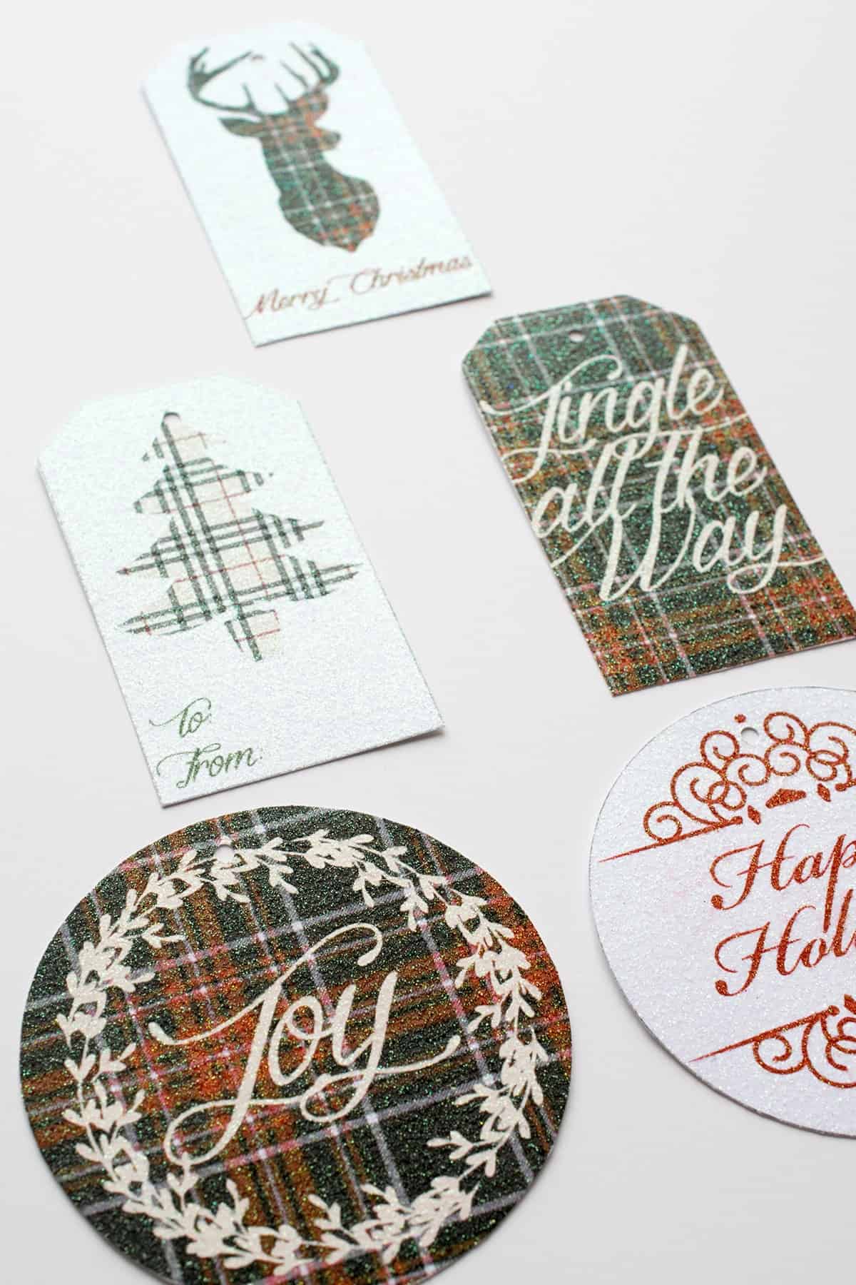 Free Printable Christmas gift tags with plaid designs and added glitter cut out on white surface. 