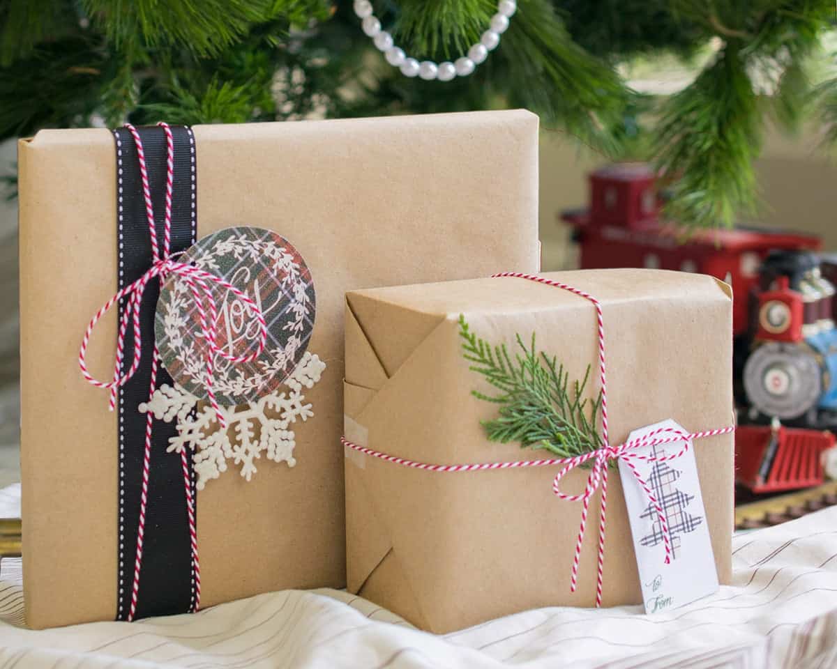Two Christmas gifts wrapped in simple brown paper with plaid ribbon and printable plaid tags beneath tree, next to train. 