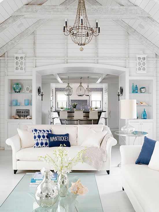 Light and bright coastal living room in white palette with blue decorative accents with view of dining room in background.