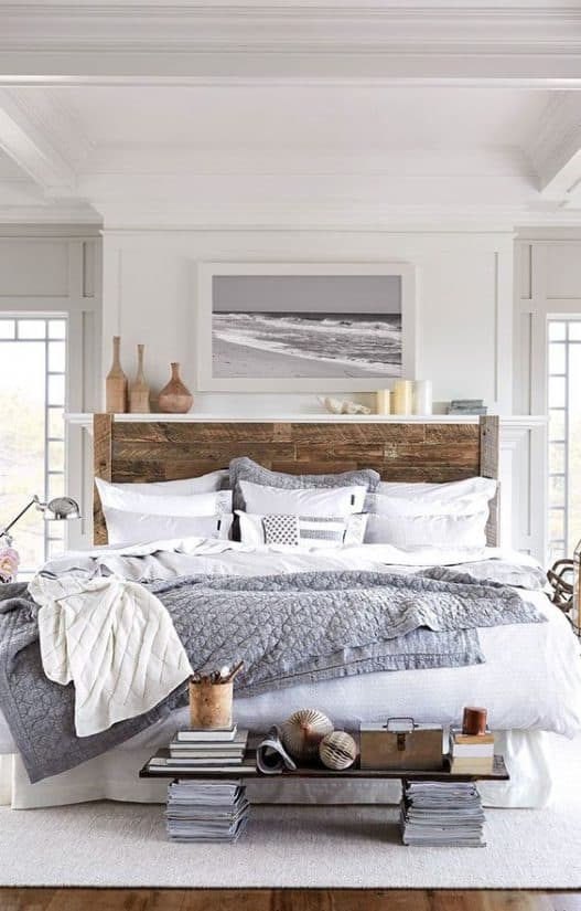 Neutral coastal bedroom decor with large wooden bed. white with gray and wood accents, black and white framed beach photo above bed.