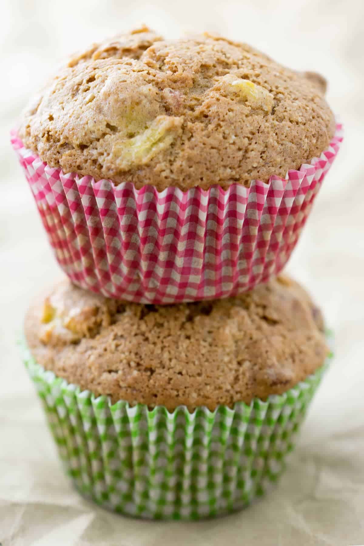Two stacked summer squash muffins with red and green liners on top of crinkled paper surface. 